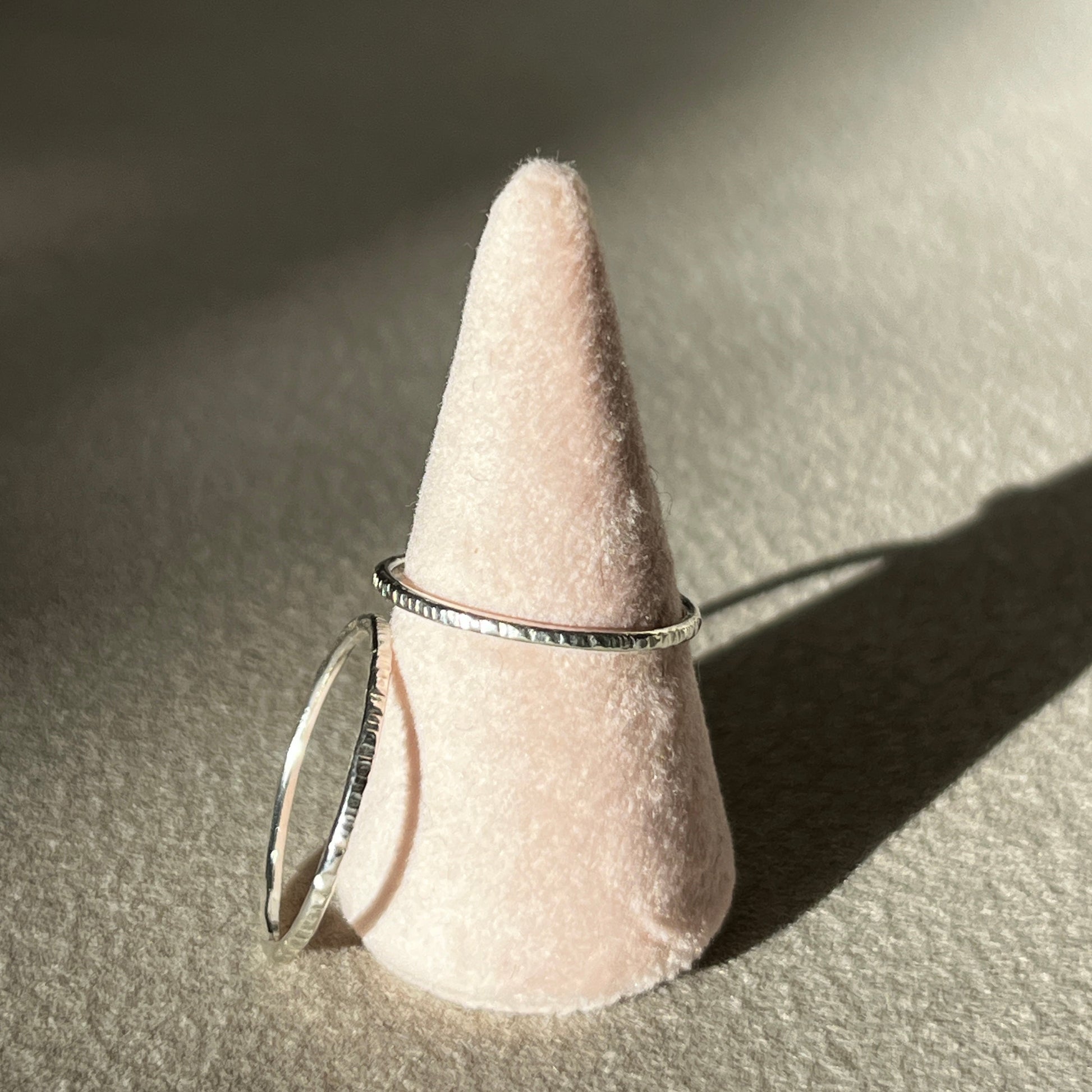 Silver ring on a cone-shaped pink stand against a neutral background