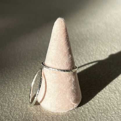 Silver ring on a cone-shaped pink stand against a neutral background