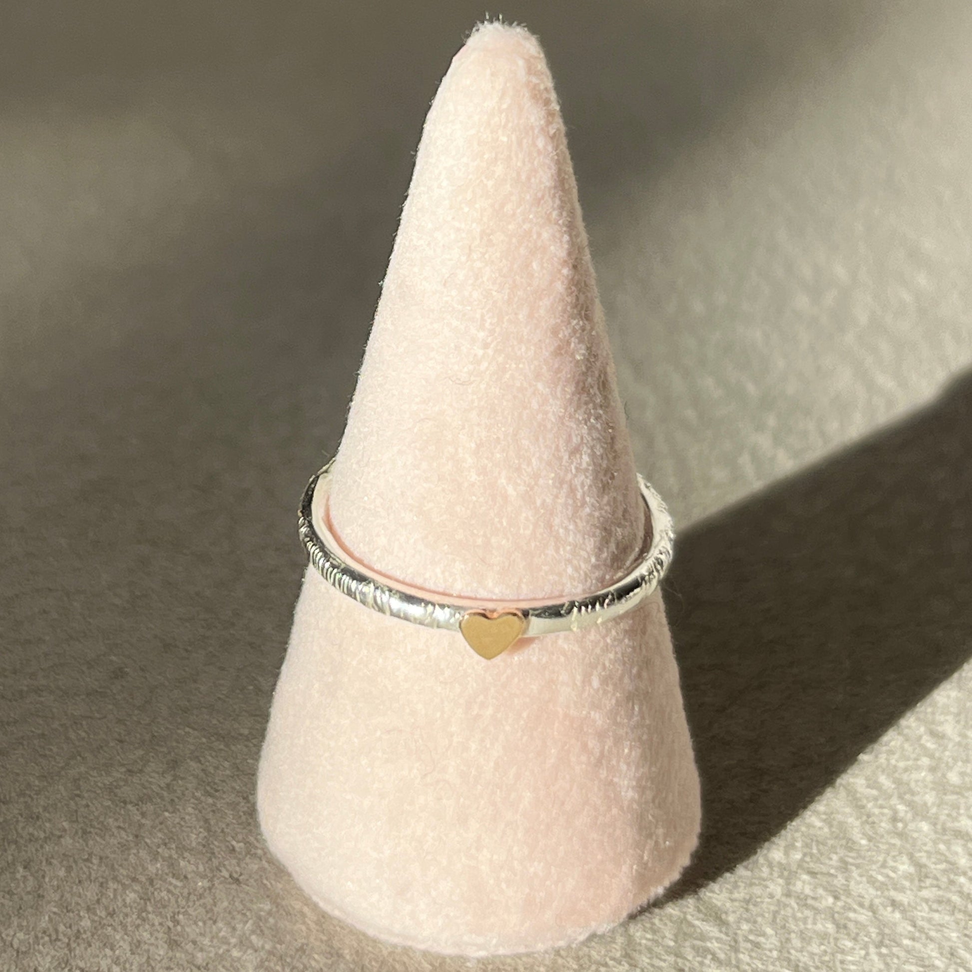 Ring on a pink cone-shaped stand with a heart detail on a beige background
