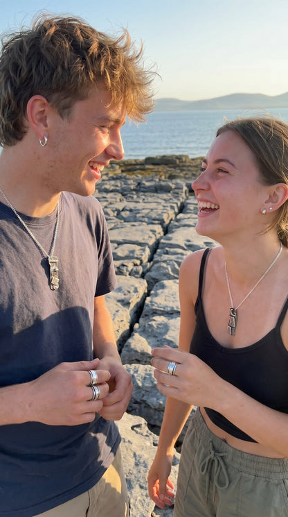Two people standing on a rocky shoreline by the ocean, smiling and laughing.