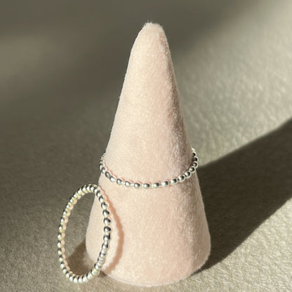 Two silver rings on a cone-shaped jewelry stand against a neutral background