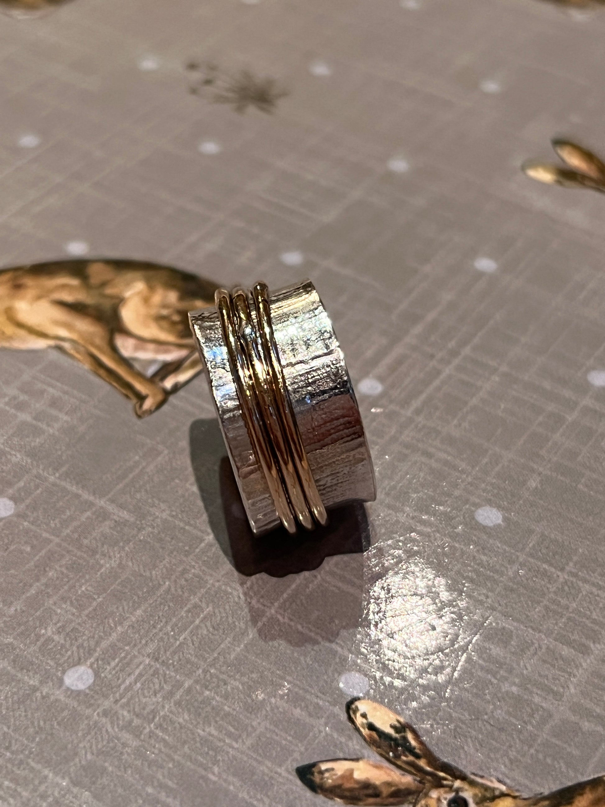 Burren sterling silver spinner textured finished with downward bark like markings finished 3 gold filled outer rings pictured on a background with rabbit pictures