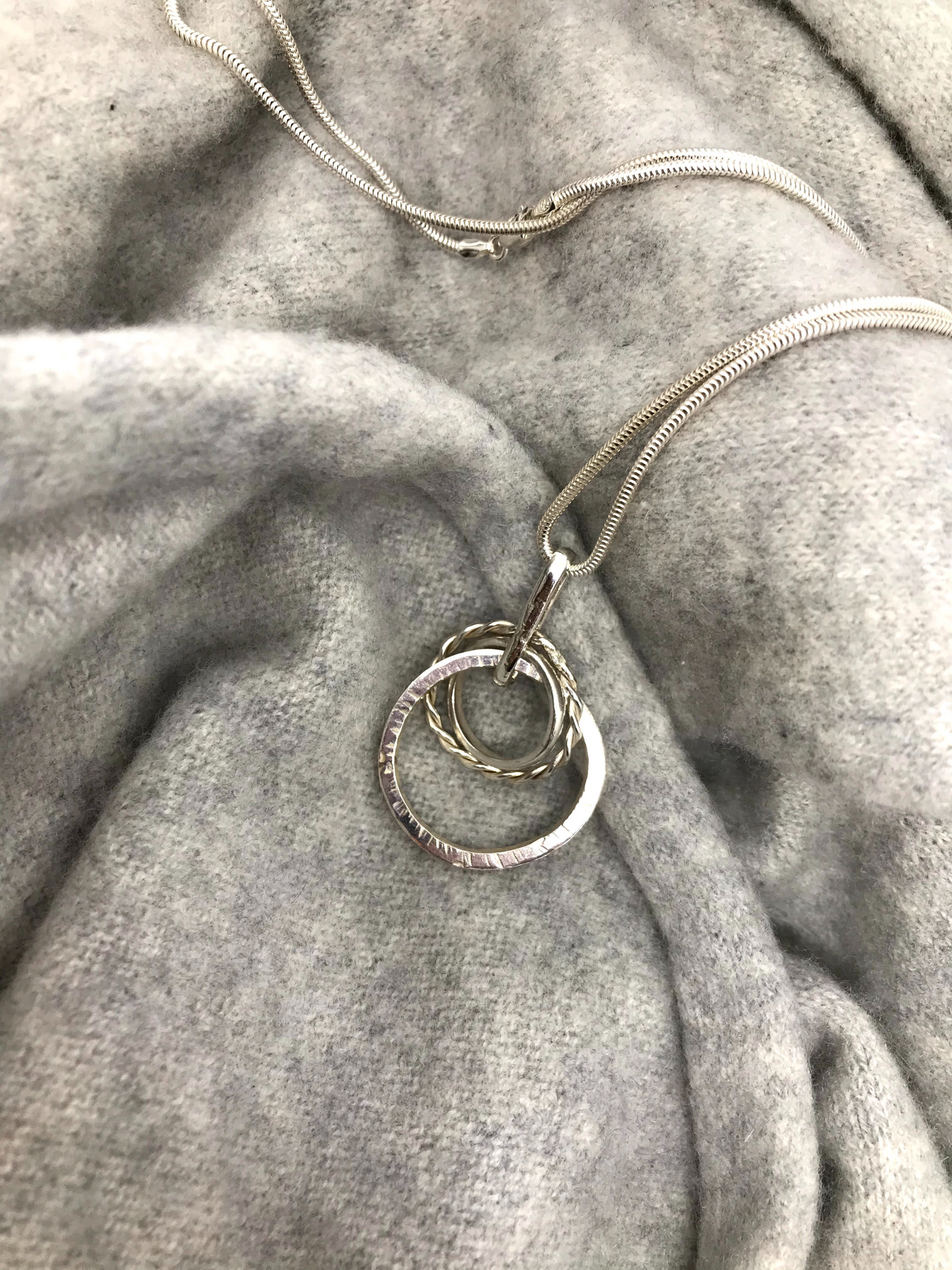 three circles intertwined twisted hammered and mirror 40cm snake chain sterling silverSterling silver mixed loop necklace.  Three circles of silver. One hammered, one twisted and one polished. Hangs on a sterling silver snake chain with a secure 'lobster claw' closing clasp.