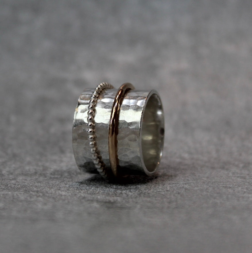 hammer finished spinner ring with a gold spinner and a silver spinner on a grey velvet box
