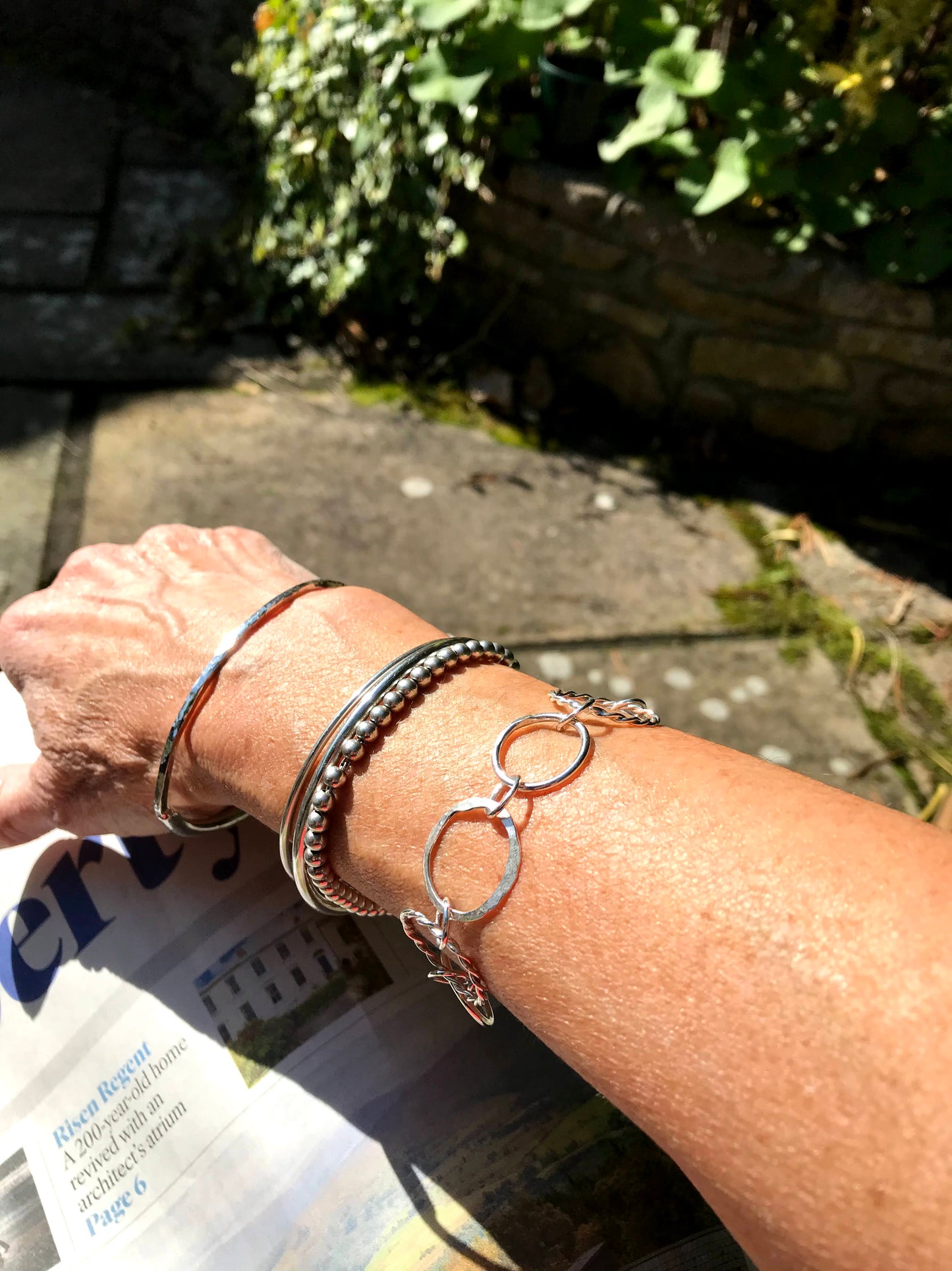 Sterling silver circles one twisted plain hammer texture connected with jumrings set on a cashmere grey background handmade jewellery jewelry handmade in Dublin Ireland arm with several bangles silver 