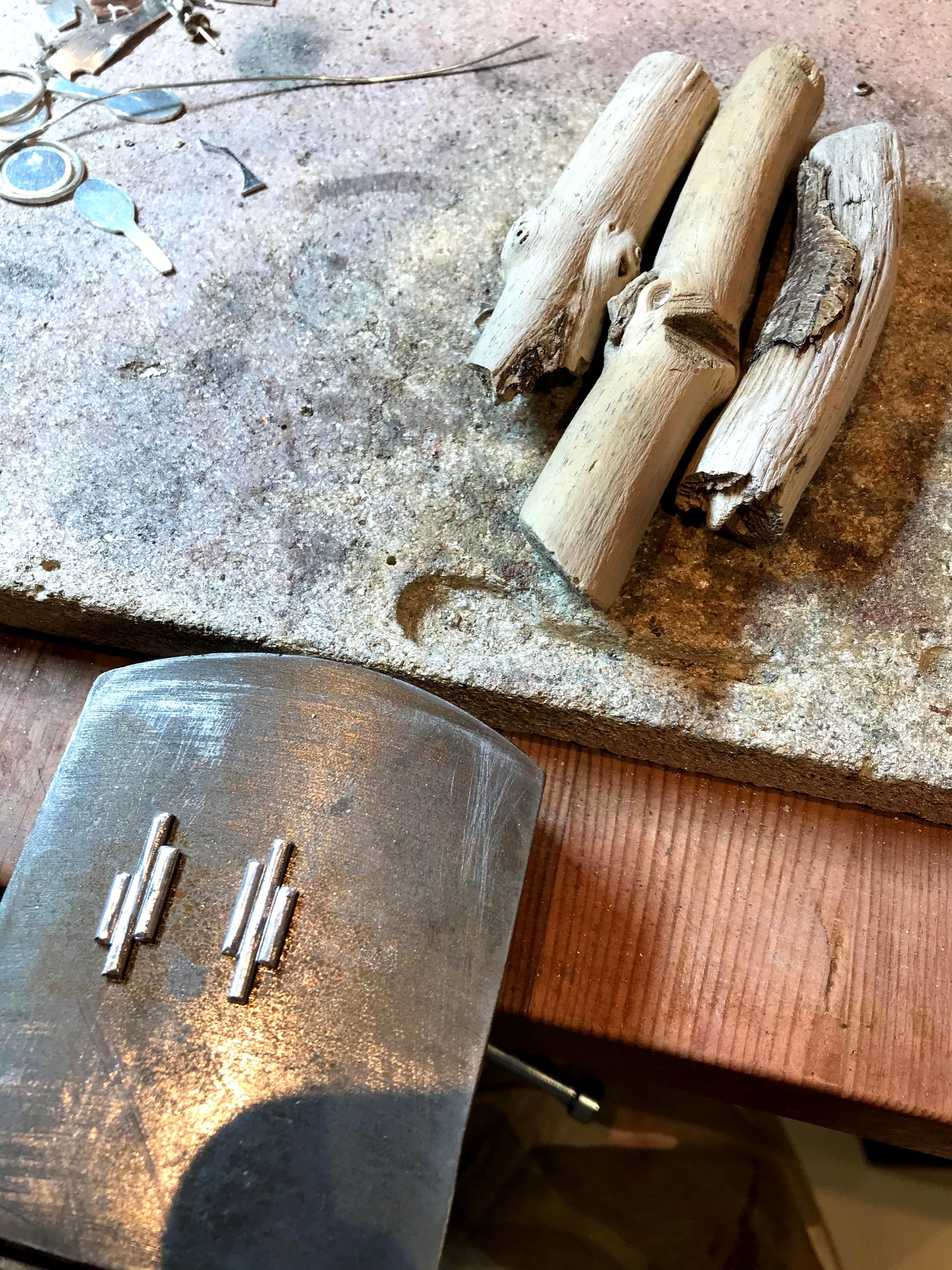 Silversmith work bench sterling silver pieces of wire for making earrings. Also shown three pieces of driftwood