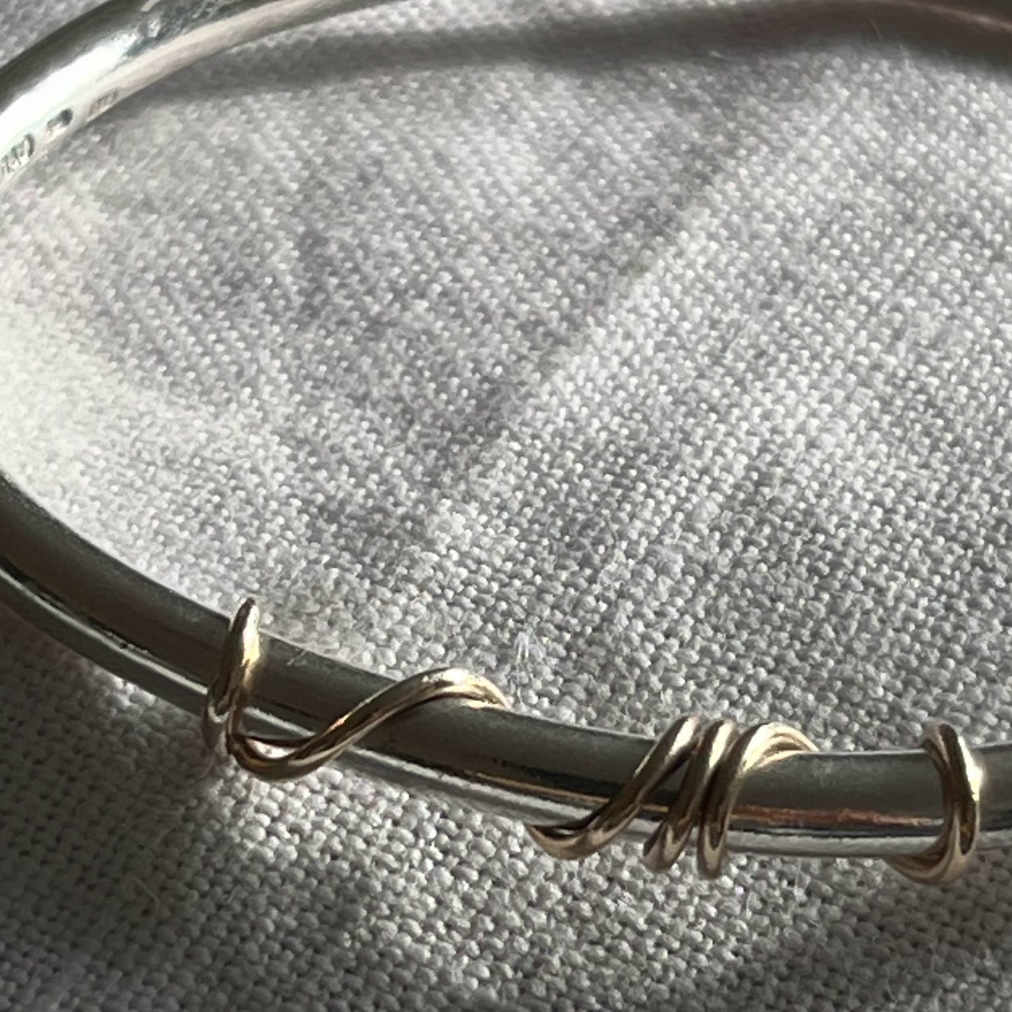 close up of handmade sterling silver solid bangle with 9ct gold wrap of wire twisted around the front of the bangle