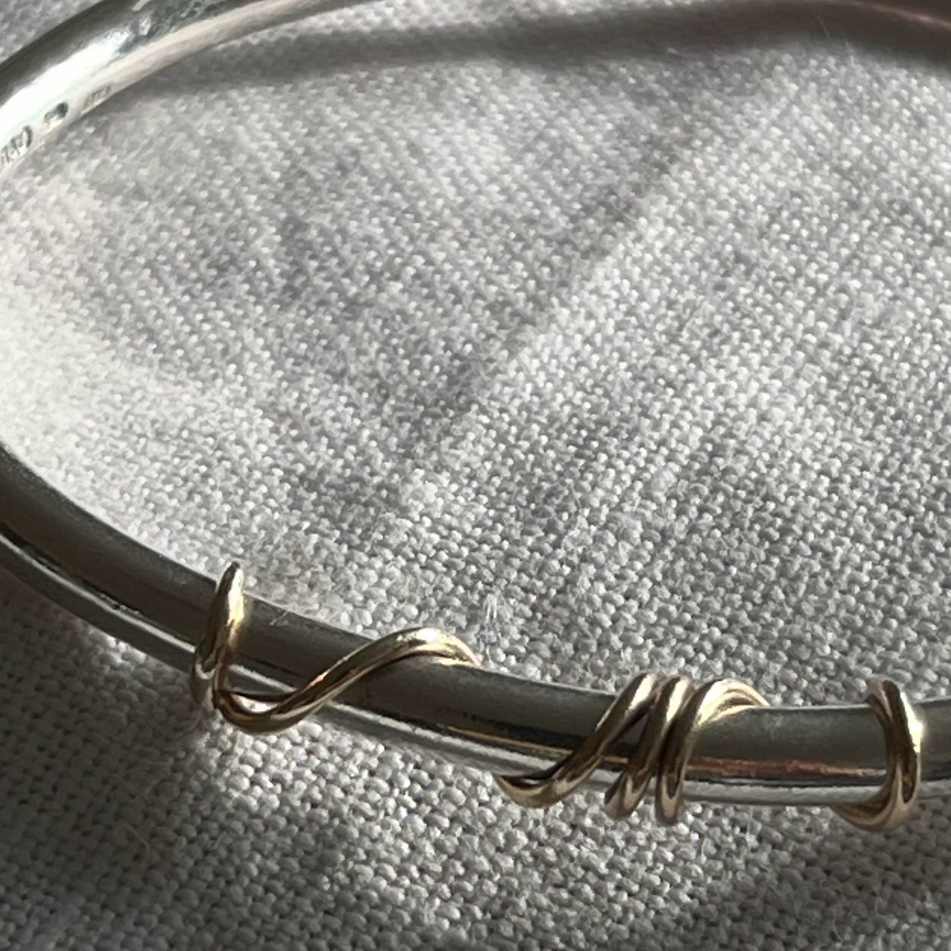 close up of handmade sterling silver solid bangle with 9ct gold wrap of wire twisted around the front of the bangle
