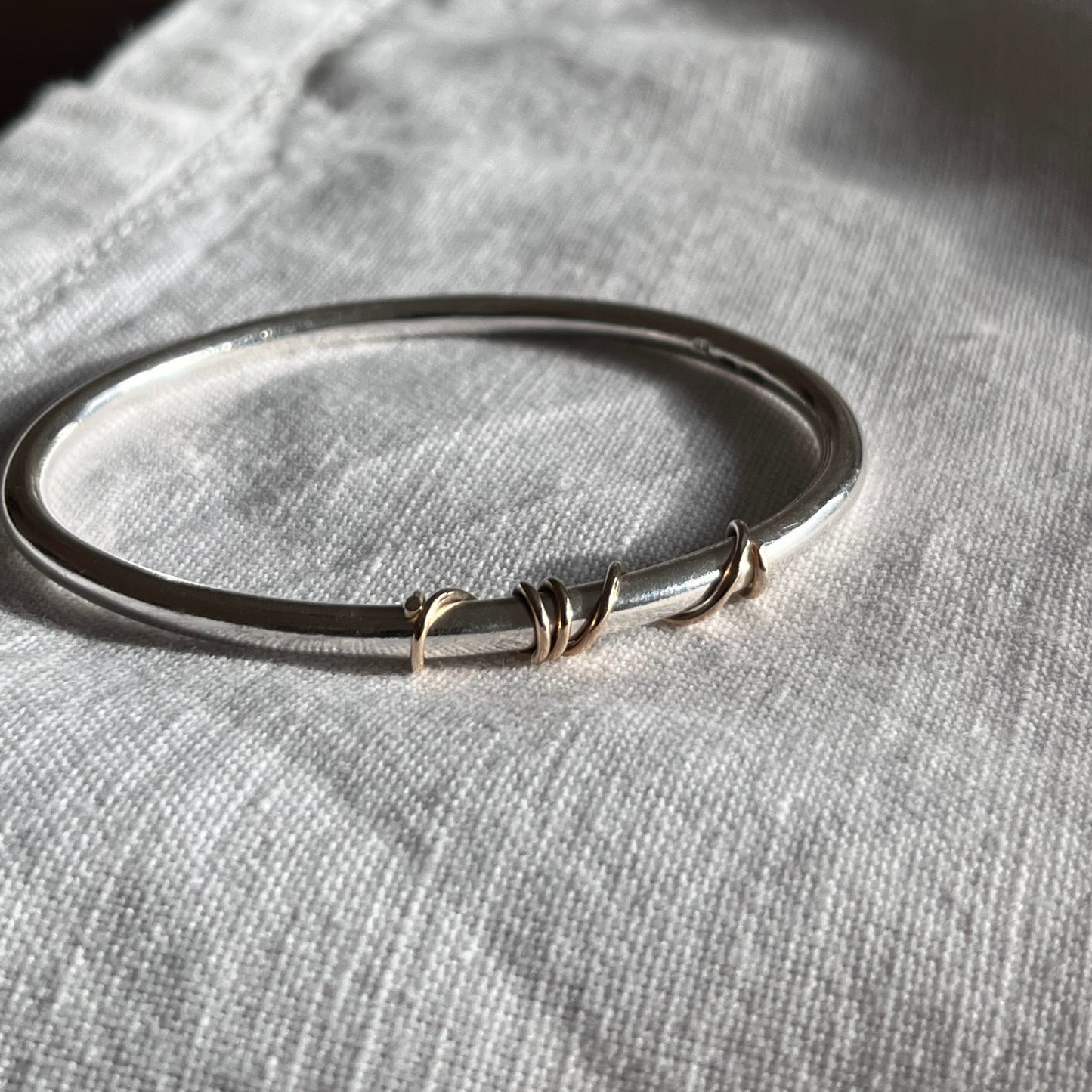 handmade sterling silver solid bangle with 9ct gold wrap of wire twisted around the front of the bangle