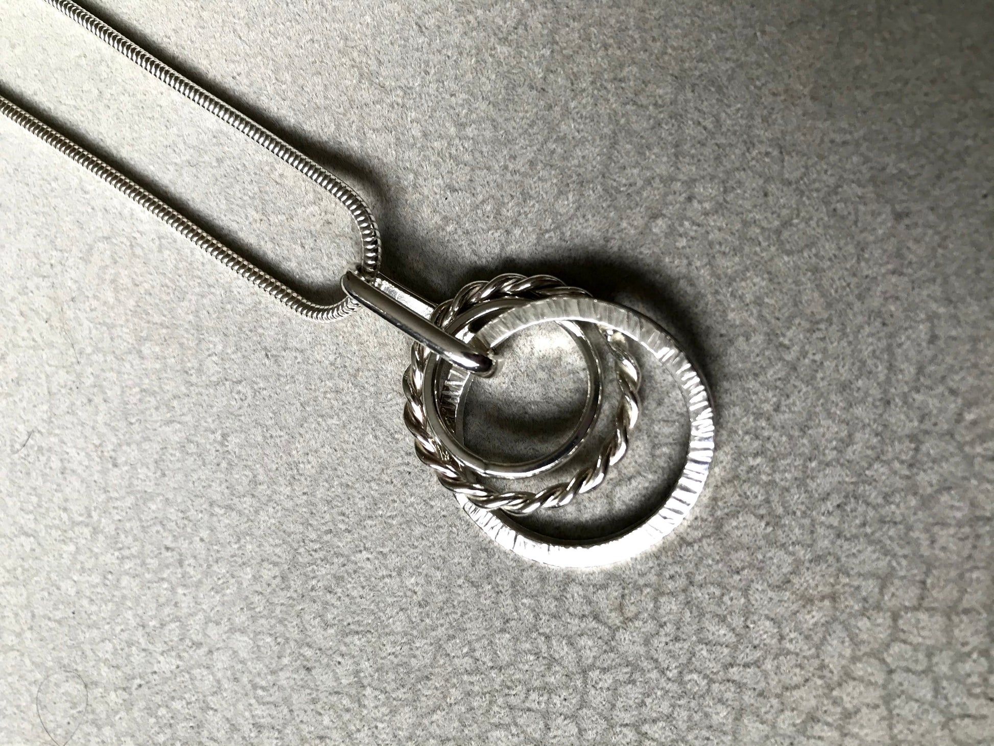 three circles intertwined twisted hammered and mirror 40cm snake chain sterling silverSterling silver mixed loop necklace. Three circles of silver. One hammered, one twisted and one polished. Hangs on a sterling silver snake chain with a secure 'lobster claw' closing clasp.