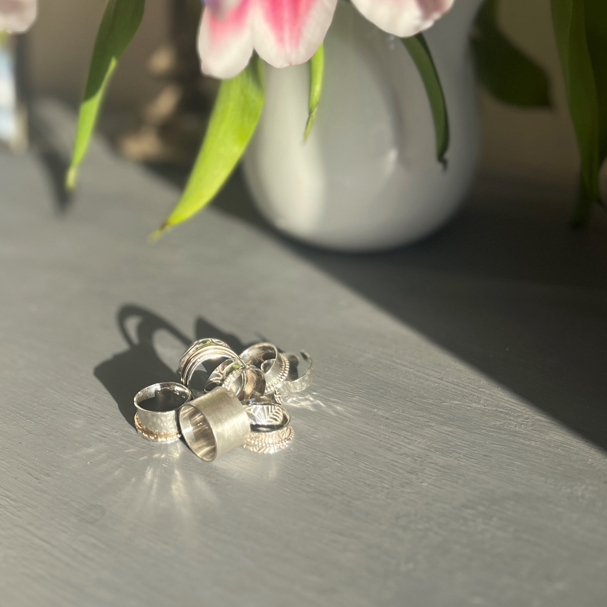 Stack of handmade silver spinner rings with a vase of flowers