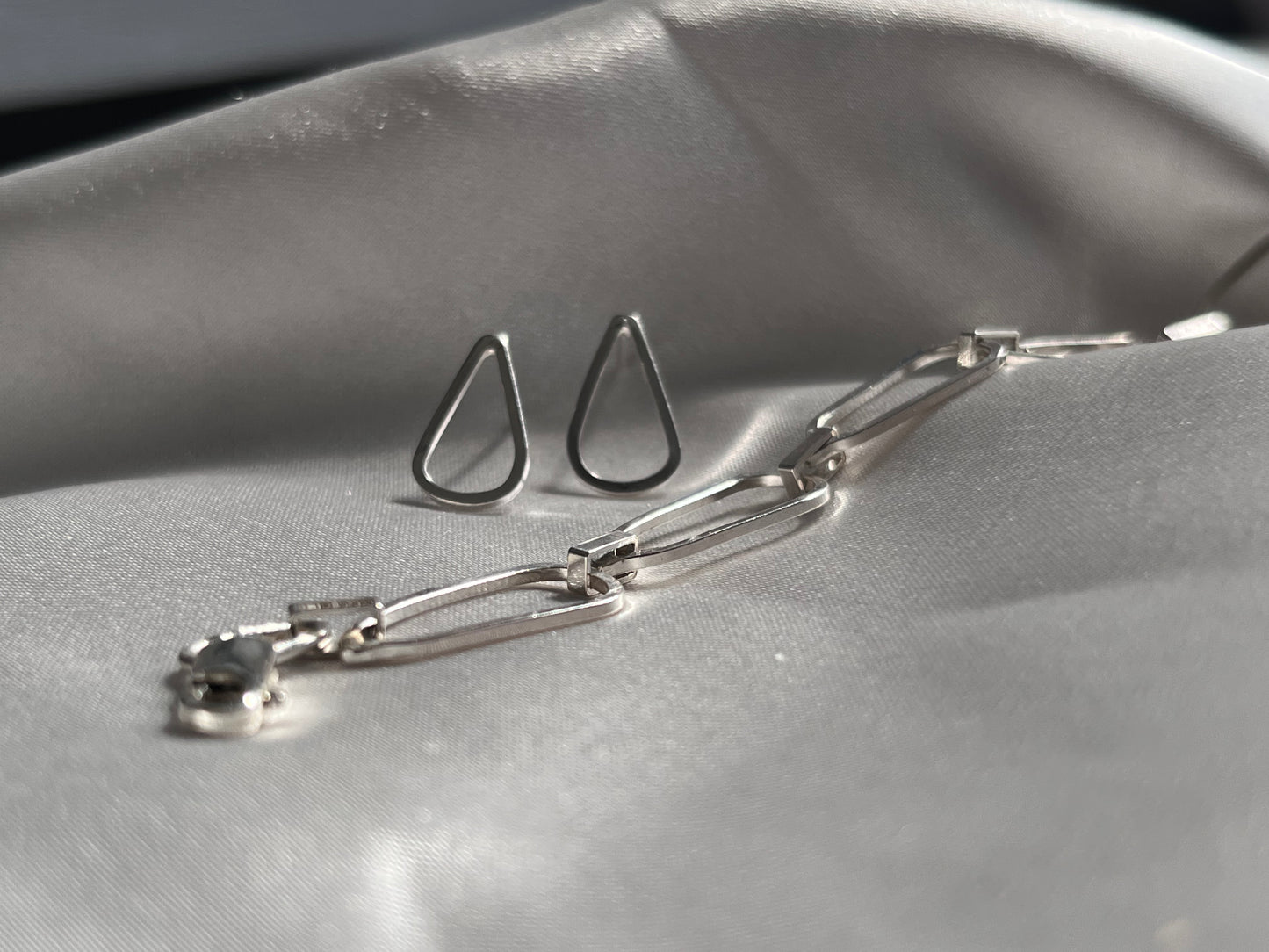 droplet shaped silver earrings with waterflow handmade silver bracelet on a grey silk background